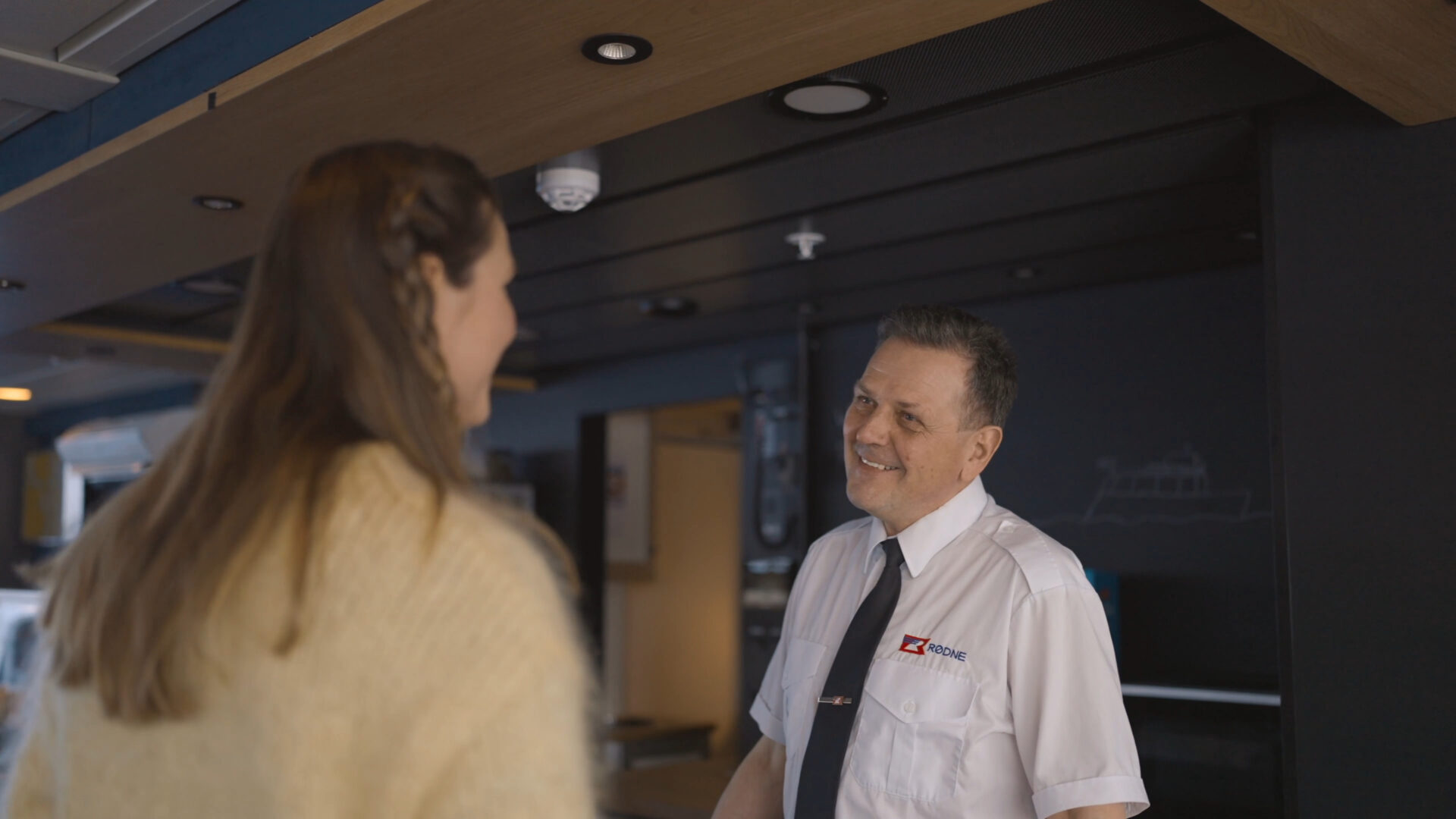 Smilende besetningsmedlem hjelper en gjest om bord på fjordcruiset.