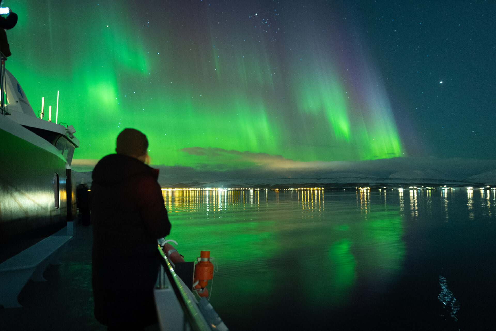 Nydelig nordlys som reflekterer i vannet ved siden av båten