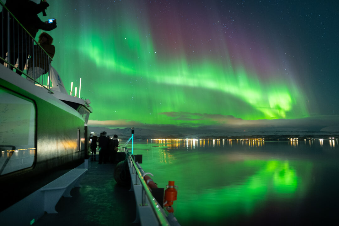 Nordlys over fjorden sett fra soldekk på båten på et Nordlystur med båt fra Tromsø