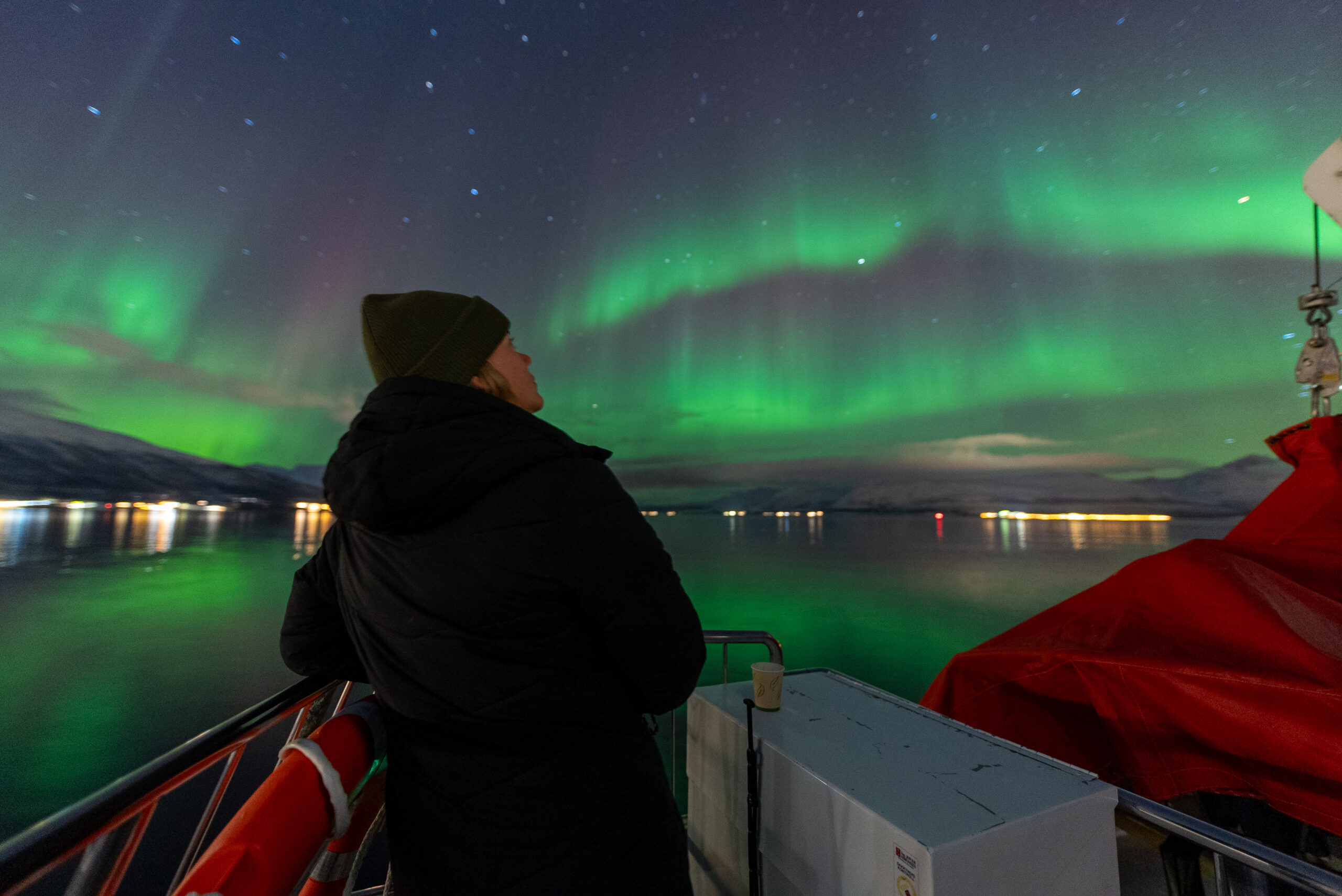 Dame som ser opp på nordlyset som danser over den stjerneklare himmelen over Tromsø by.