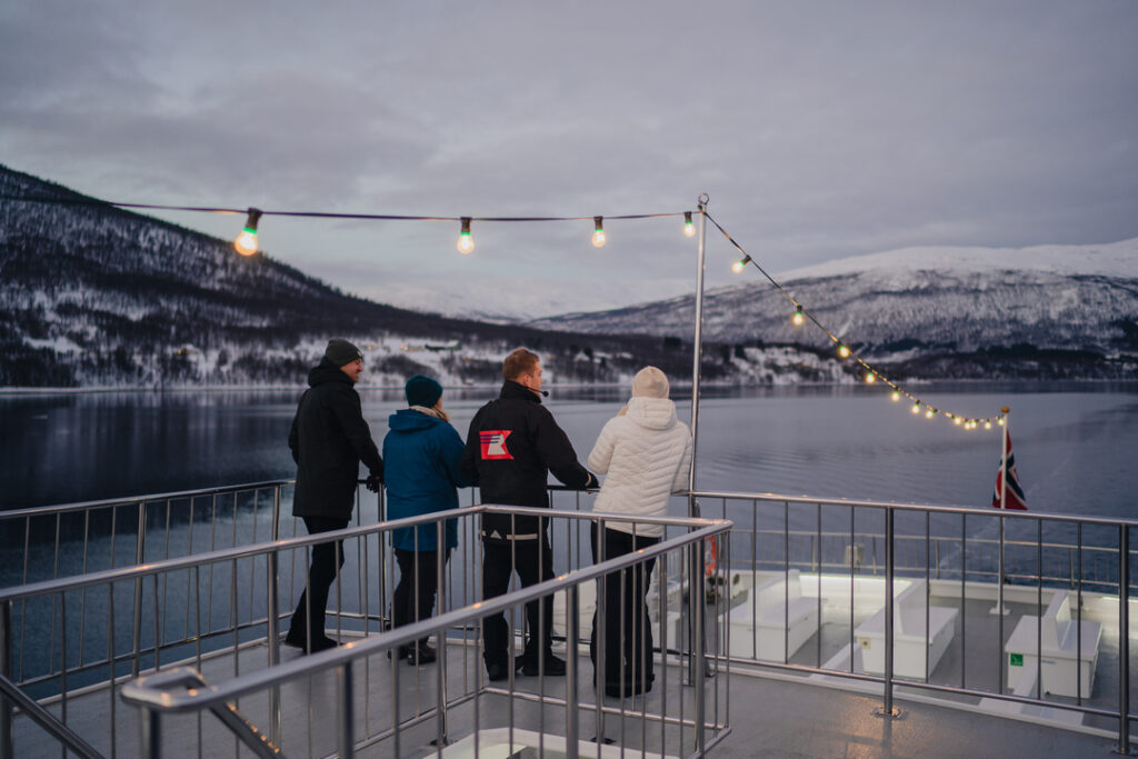 Tre gjester og en Rødnes-guide speider etter hval i fjordene utenfor Tromsø under hvalsafari.