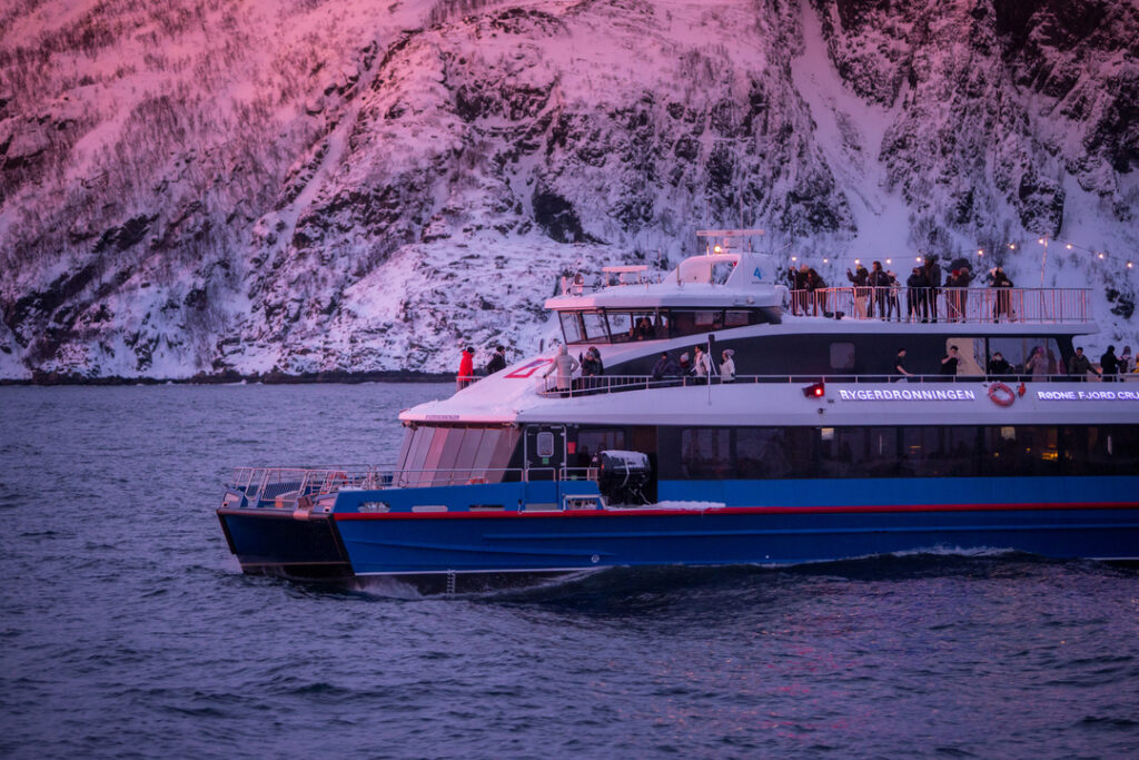Katamaran på hvalsafari fra Tromsø i det flotte polarlyset som gir en lys rosa himmel.
