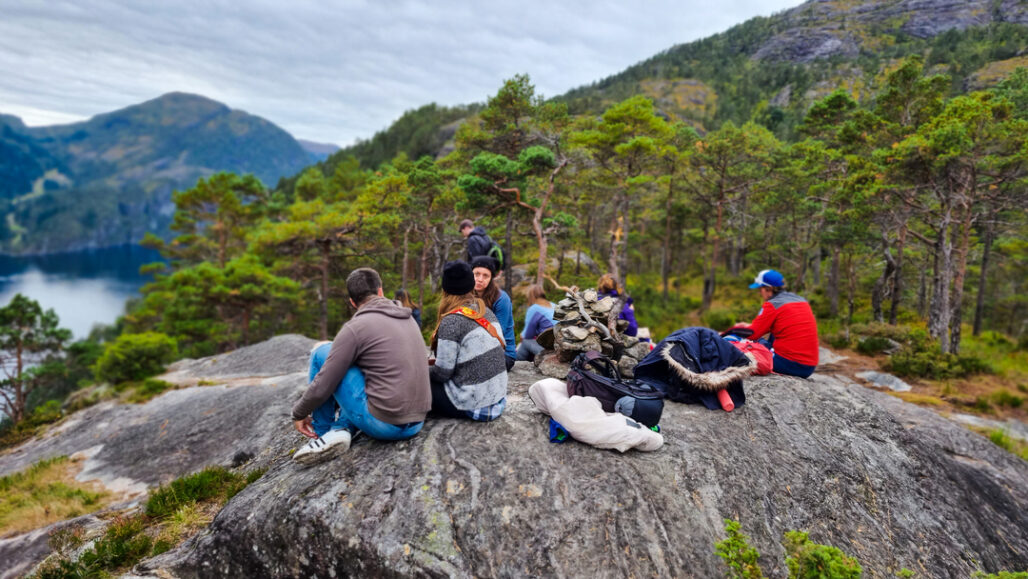 Etter en fantastisk fjelltur opp til Slottet tar en gruppe turgåere en velfortjent lunsjpause med panoramautsikt over fjorden. En perfekt dag i Bergens vakre fjellandskap!