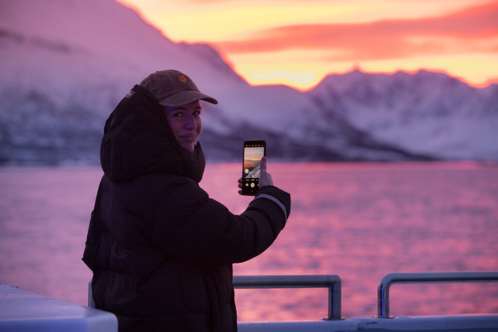 Smiling guest taking a photo of Lyngen Alps during a Tromsø whale watching cruise