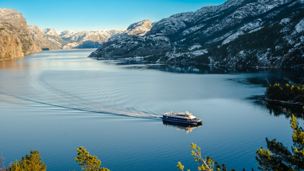 Fjordcruisebåt seiler gjennom Lysefjorden med speilblankt vann og dramatiske fjell.