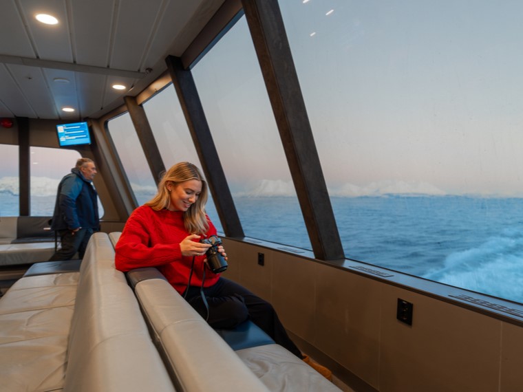 Girl enjoying the big panoramic windows and looking through her photos from the Arctic fjord cruise in Tromsø