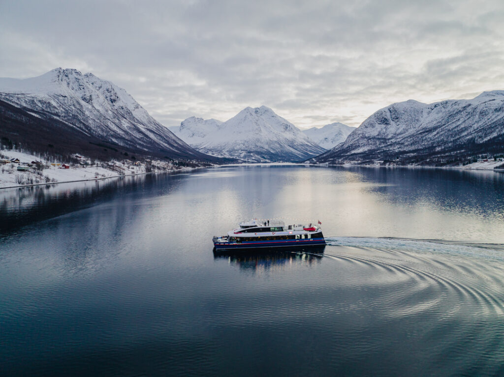 A stunning aerial view of a fjord near Tromsø, with calm water, snow-covered peaks, and the vast Arctic landscape from above.
