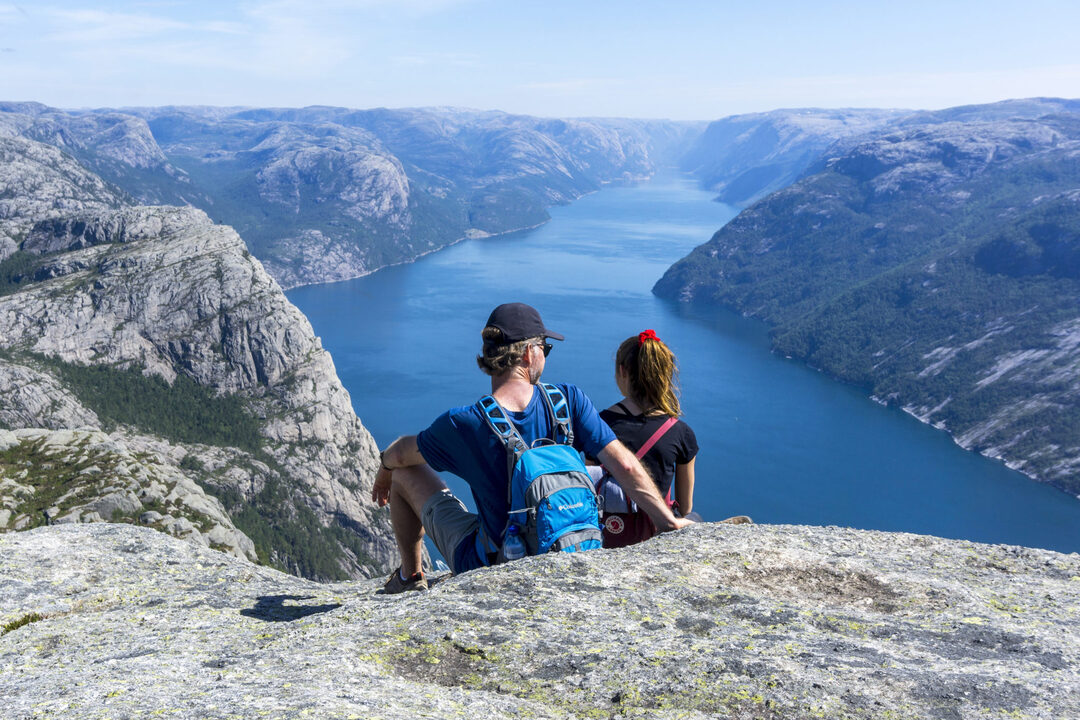A couple sitting at the edge of Preikestolen enjoying the views of the Lysefjord towards the Lysebotn.