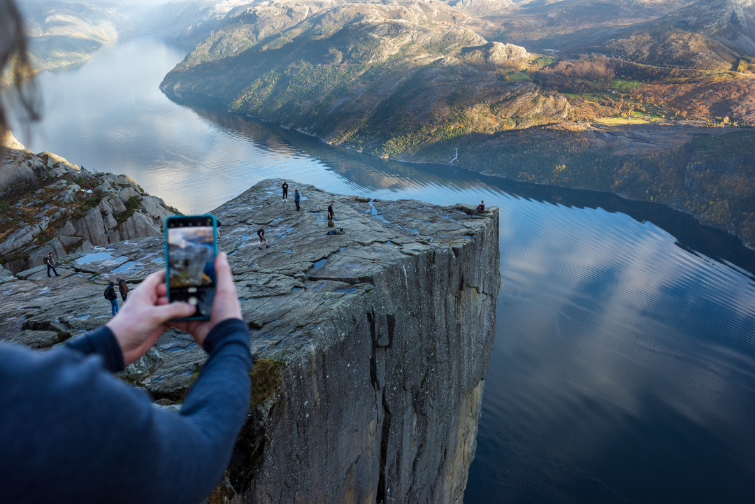 A hiker takes a photo of the pulpit Rock - Preikestolen and the winding lysefjordfjord in the background.