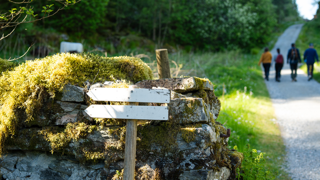 And old stone wall and trail signs along the hike path in Kossdal, 4 hikers in the background.