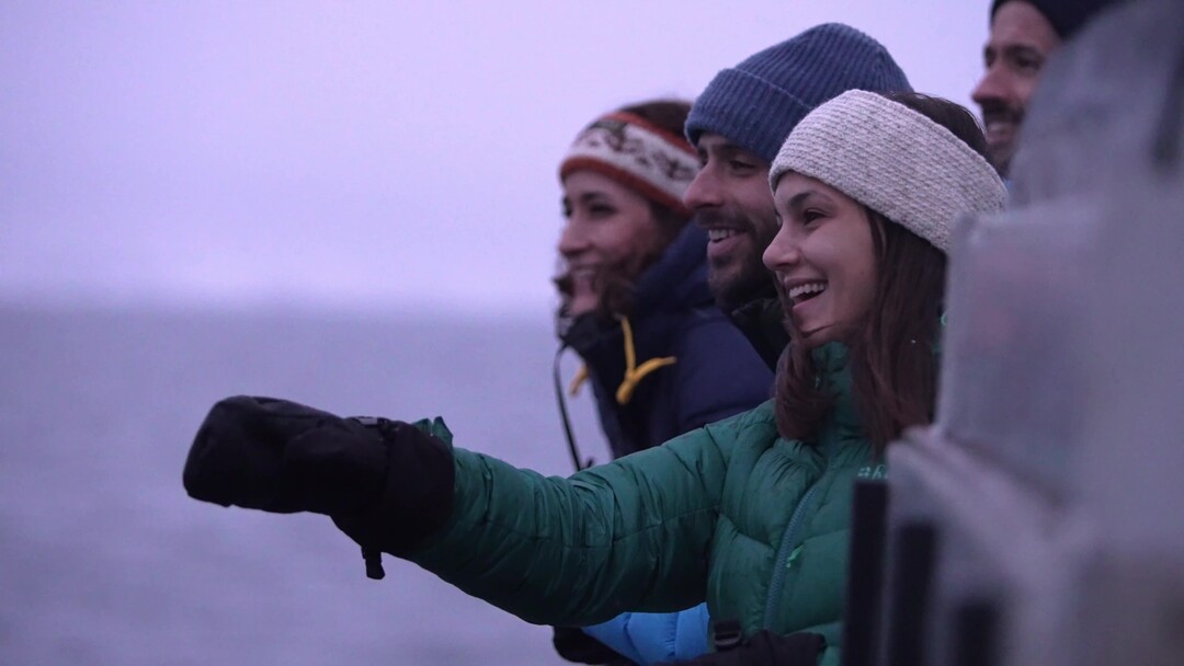 A woman smiling and pointing towards the whales surfacing just outside the boat on a Rødne Whale safari in Northern Norway