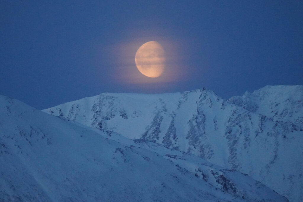 The Moon rising above the peaks of Lyngen Alps in Northern Norway, highlighting Arctic mountain landscapes at polar night.