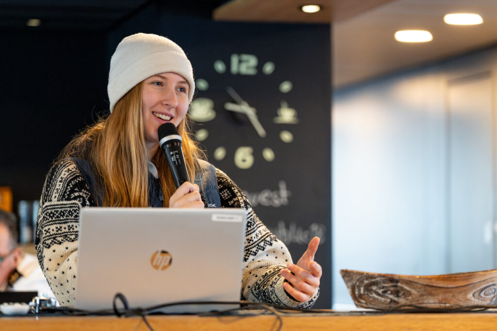 Close-up of a Rødne guide explaining details on a Tromsø fjord cruise, engaging with guests on deck with Arctic waters in the background.