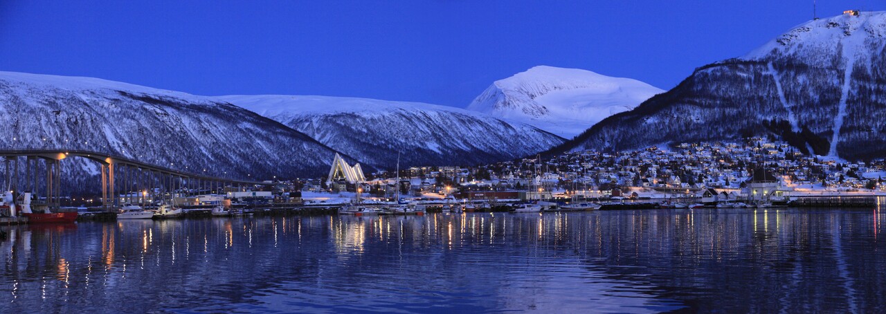 Panoramic view of Tromsø’s Arctic Cathedral and city bridge during the blue hour of the polar night, with soft Arctic light reflecting on the calm water.