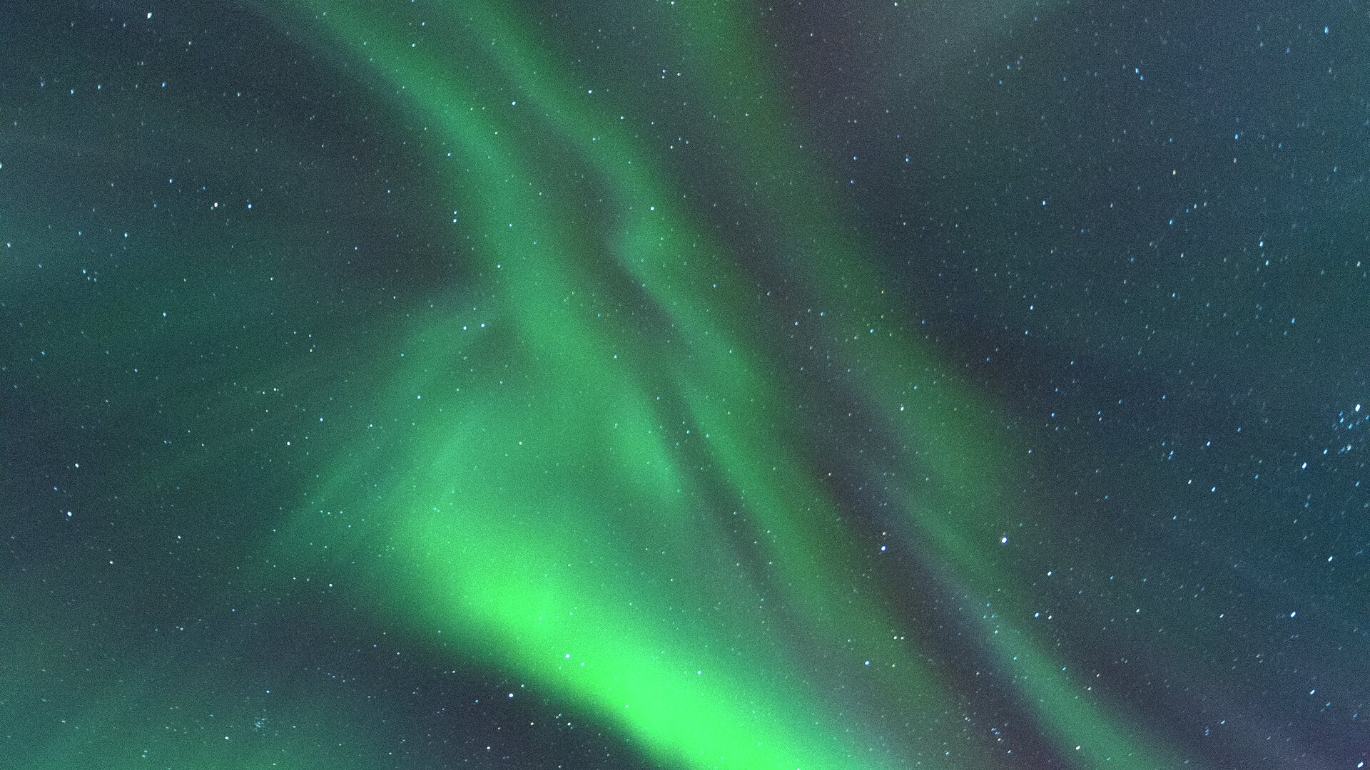 Bright green Northern Lights stretching across a clear, star-filled Arctic night sky.